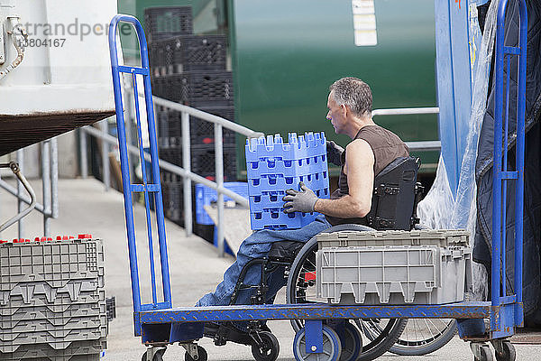 Laderampenarbeiter mit Rückenmarksverletzung im Rollstuhl beim Bewegen von gestapelten Inventartabletts