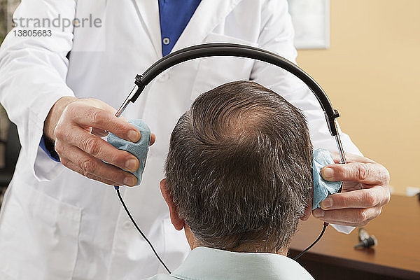 Ein Audiologe setzt einem Patienten zur audiometrischen Untersuchung ein Headset auf