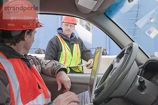 Ingenieur arbeitet in einem Lastwagen an einem Laptop und bespricht Daten mit einem anderen Ingenieur