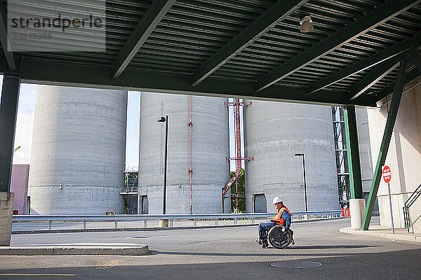 Techniker im Rollstuhl bei der Inspektion von Lagertanks im Freien