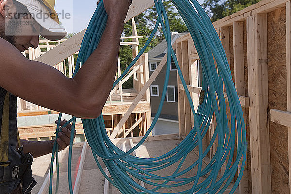 Ein spanischer Zimmermann wickelt einen Luftschlauch an einem im Bau befindlichen Haus ab