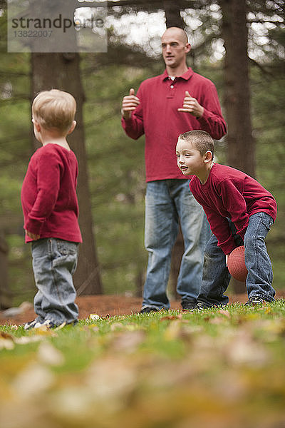Mann gebärdet das Wort ´Play´ in amerikanischer Zeichensprache  während er mit seinen Söhnen in einem Park spielt