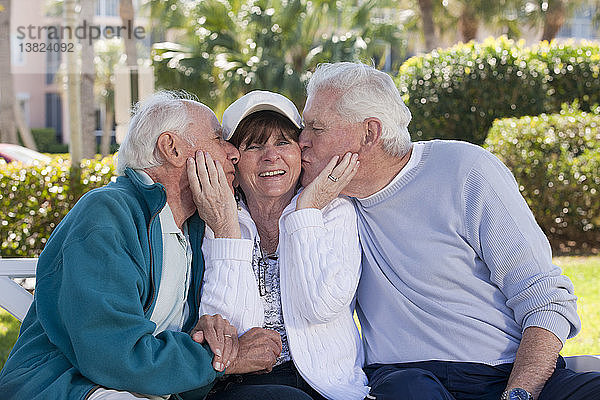 Zwei ältere Männer  die ihre Freundin in einem Park küssen
