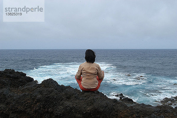 Meditierende Frau mit Blick auf den Atlantischen Ozean