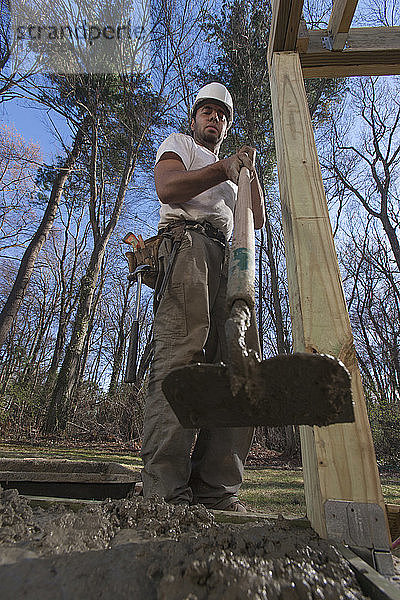 Hispanischer Zimmermann beim Nivellieren von Beton im Treppenfundament