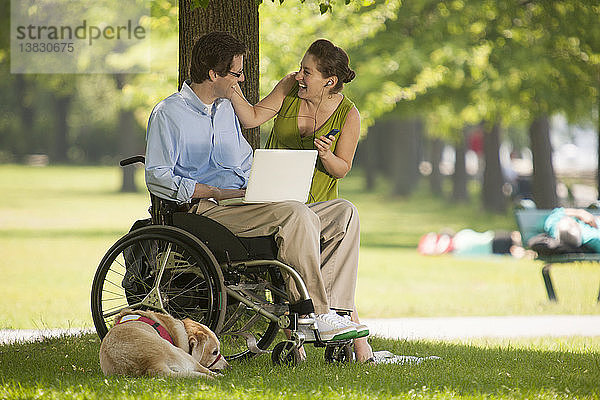 Mann im Rollstuhl mit schwangerer Frau genießt Elektronik in einem Park