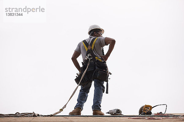 Ein hispanischer Zimmermann steht mit Hammer  Kreissäge und Nagelpistole auf dem Dach