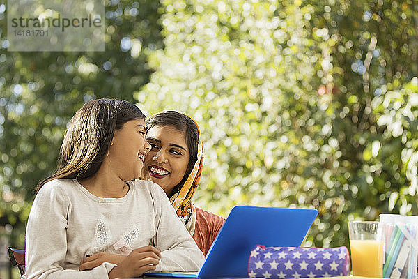 Glückliche Mutter und Tochter mit Laptop auf der Terrasse