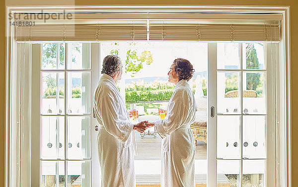 Älteres Paar in Wellness-Bademänteln trinkt Mimosen an der Terrassentür des Hotels