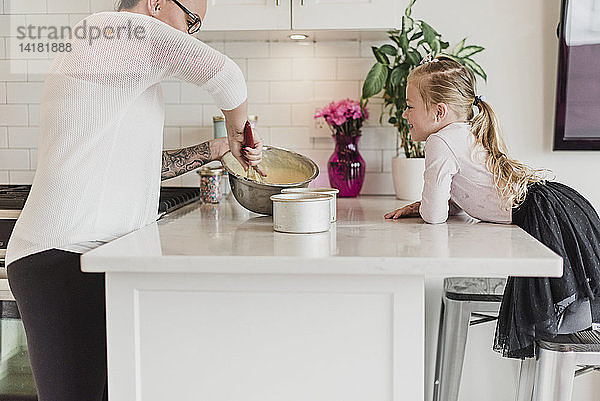 Neugieriges Mädchen beobachtet Mutter beim Backen in der Küche