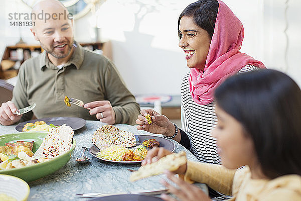 Glückliche Frau im Hidschab beim Abendessen mit der Familie am Tisch