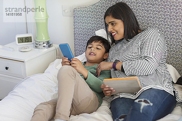 Mutter und Sohn benutzen Smartphone und Tablet auf dem Bett