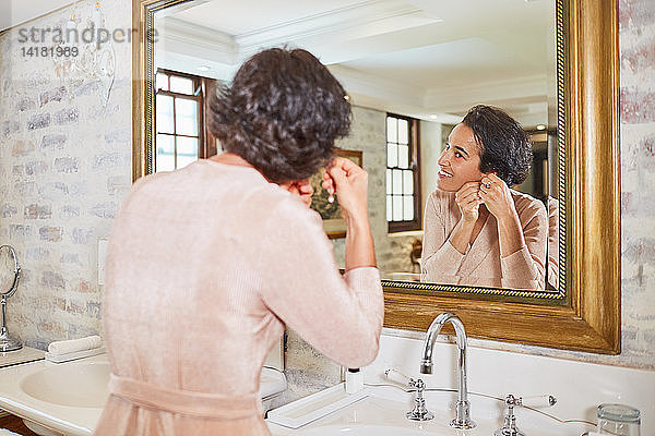 Frau beim Anlegen von Ohrringen vor dem Badezimmerspiegel eines Hotels