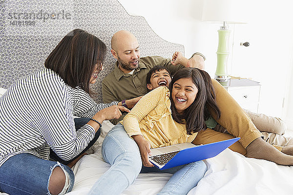 Verspielte Familie mit Laptop auf dem Bett
