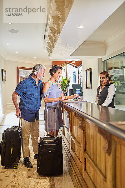 Älteres Paar mit Koffern beim Einchecken an der Hotelrezeption