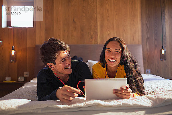 Porträt eines glücklichen Paares mit Kopfhörern und gemeinsamem Laptop auf dem Bett