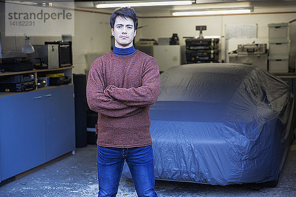 Porträt eines selbstbewussten Mannes vor einem abgedeckten Auto in einer Garage