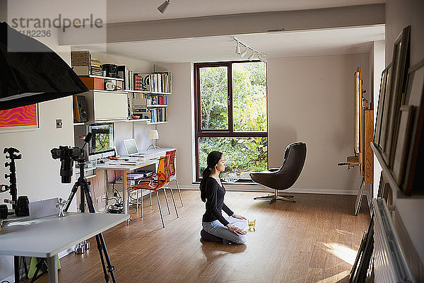 Junge Frau meditiert auf dem Boden im Heimbüro