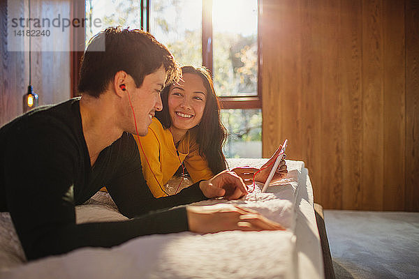 Lächelndes Paar mit Kopfhörern  das sich ein digitales Tablet im Bett teilt