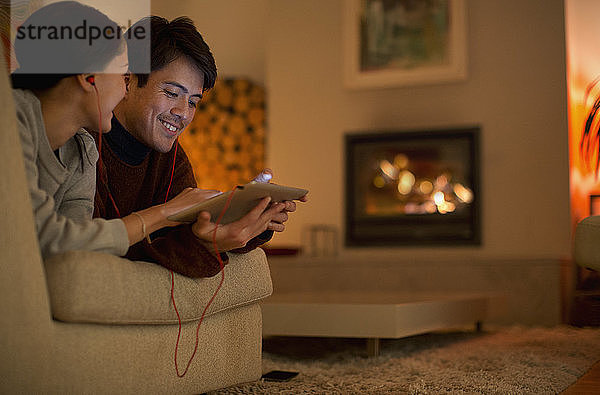 Glückliches Paar mit Kopfhörern und digitalem Tablet auf dem Wohnzimmersofa