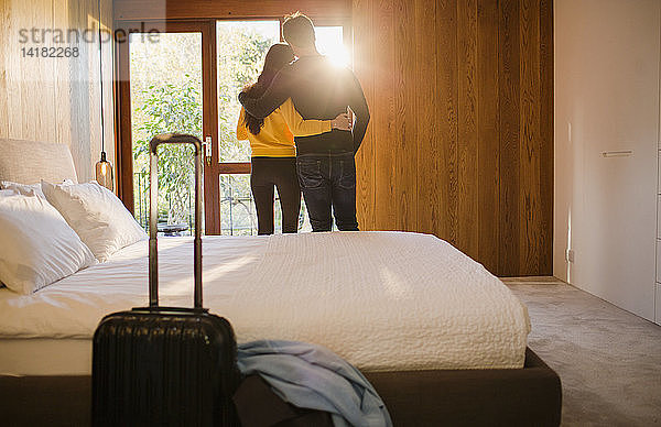 Paar mit Koffer  das sich im Schlafzimmer umarmt