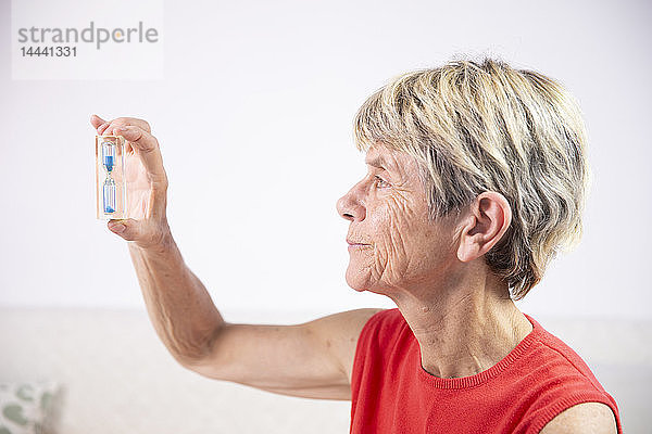 Alte Frau schaut auf eine Sanduhr