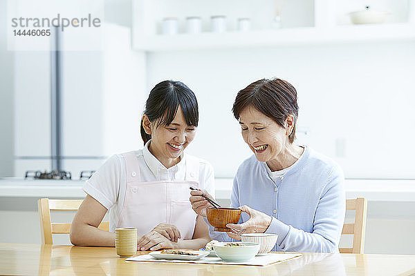 Junge japanische Pflegerin kümmert sich um älteren Patienten