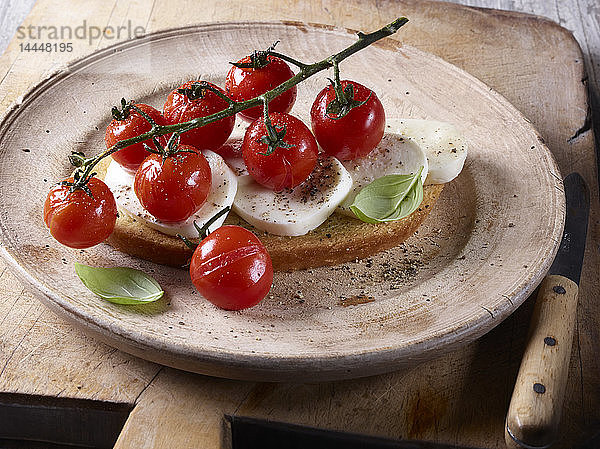 Eine Scheibe Brot  belegt mit Tomaten  Mozzarella und Basilikum