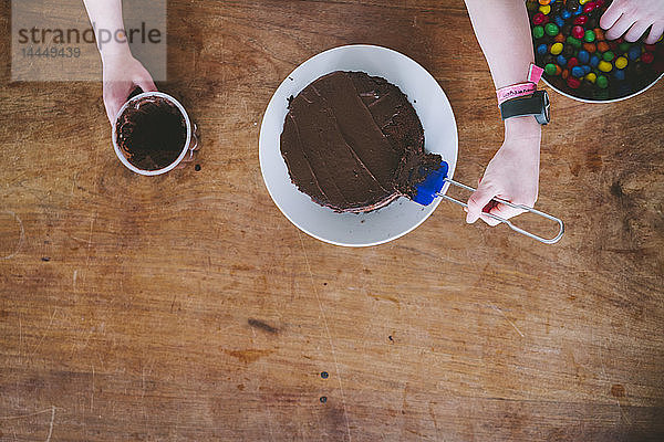 Zwei Kinder backen Schokoladenkuchen zum Muttertag von oben an einem Holztisch