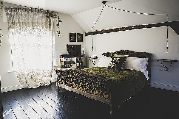 Innenansicht des Dachgeschoss-Schlafzimmers mit dunklem Holzfußboden und weißen Wänden  antikes französisches Doppelbett mit grünem Überwurf und Spitzennetzvorhang im Fenster.