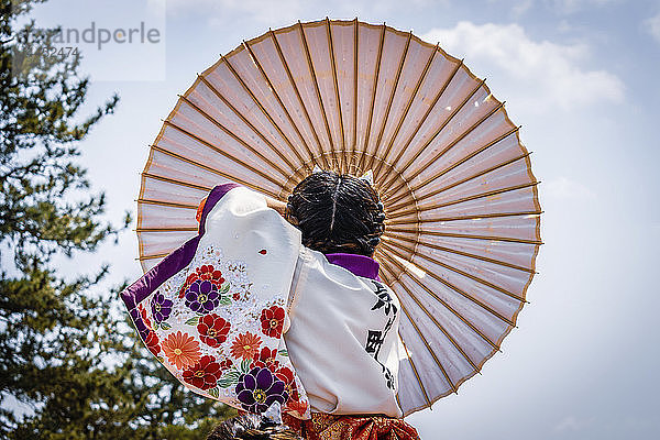 Japanisches Mädchen trägt traditionellen Regenschirm während eines Frühlingsfestes.