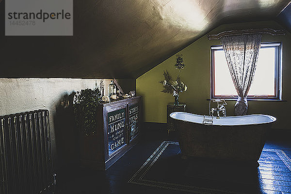Innenansicht des Dachbodenbadezimmers mit Holzboden  grünen Wänden und Kupferdecke  freistehender Badewanne mit Kupferpantoffeln und Vintage-Schrank.