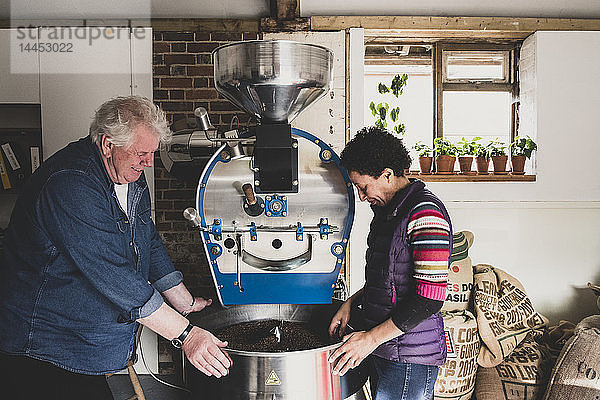 Mann und Frau stehen neben dem Kaffeeröster und kontrollieren die Kaffeebohnen.