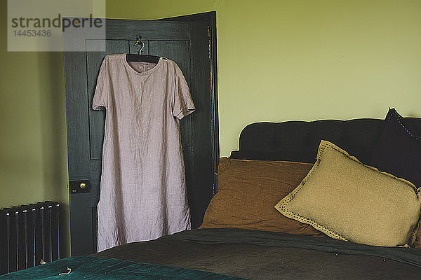 Innenansicht des Schlafzimmers mit hellgrünen Wänden  Doppelbett mit und zartrosa Leinennachthemd auf Kleiderbügel über der Tür.