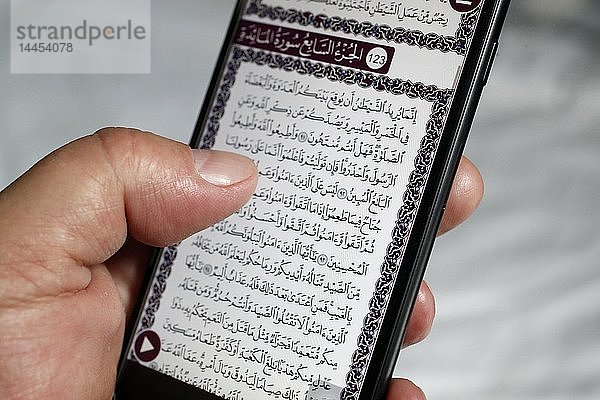 Ein Mann liest einen elektronischen Koran auf einem Smartphone.