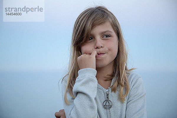 Porträt eines ausdrucksstarken  hübschen kleinen Mädchens  das bei Einbruch der Dunkelheit vor dem Meer nachdenkt.