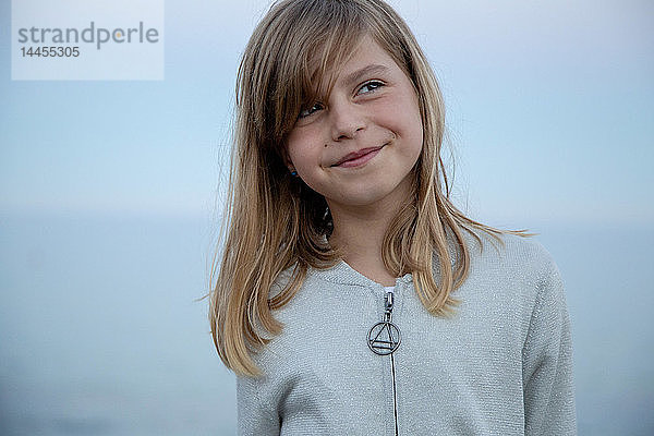 Porträt eines ausdrucksstarken  hübschen kleinen Mädchens vor dem Meer bei Einbruch der Dunkelheit.