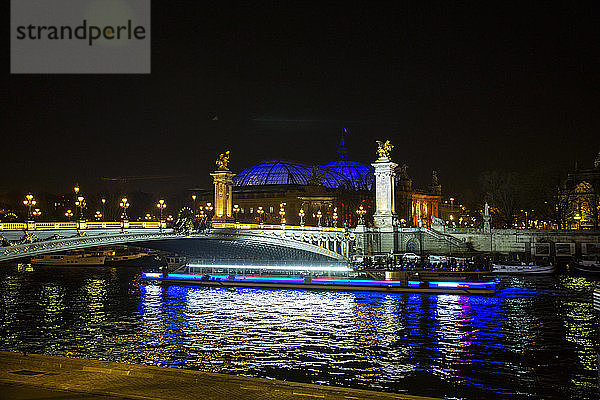 Nachtansicht eines Flugbootes  das die Seine vor dem Grand Palais mit seiner beleuchteten Kuppel und der beleuchteten Brücke Alexandre III in Paris  Frankreich  überquert.