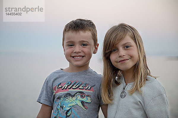 Ein kleines Mädchen und ihr Bruder posieren zärtlich vor dem Meer bei Einbruch der Dunkelheit.
