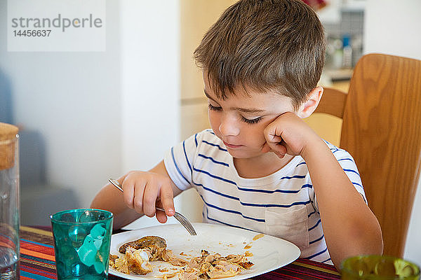 Kleiner Junge  der am Tisch sitzend Kartoffeln und Huhn isst.