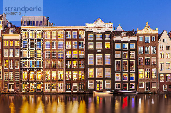 Niederländische Giebel an einer Reihe typischer Amsterdamer Häuser bei Nacht mit Spiegelungen im Damrak-Kanal  Amsterdam  Nordholland  Niederlande