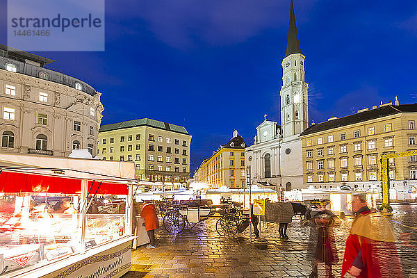 Blick auf Weihnachtsmarktstände und die katholische Kirche St. Michael am Michaelerplatz in der Abenddämmerung  Wien  Österreich