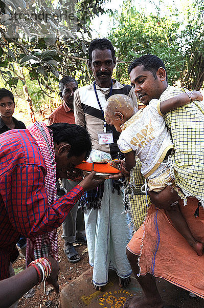 Ein Stammesangehöriger der Mali bietet dem Tempelpundit ein Puja-Geschenk an  nachdem er seinem Kind beim Shivraatri-Fest den Kopf rasiert hat  Koraput  Odisha  Indien