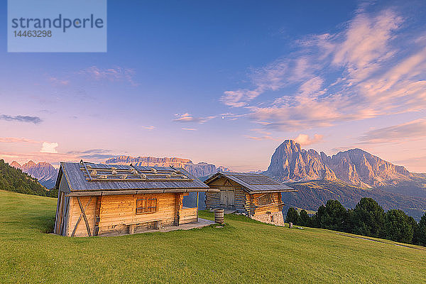 Traditionelle Hütten bei Sonnenuntergang mit Langkofel und Sellagruppe im Hintergrund  Grödnertal  Südtirol  Dolomiten  Italien