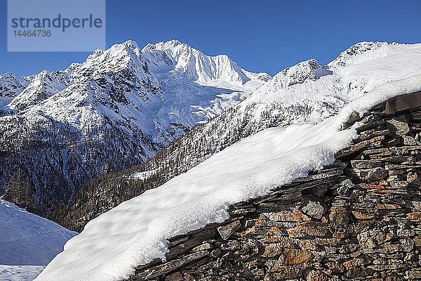 Mit Schnee bedeckte Steinhütte mit dem Monte Disgrazia im Hintergrund  Alpe dell'Oro  Valmalenco  Valtellina  Lombardei  Italien