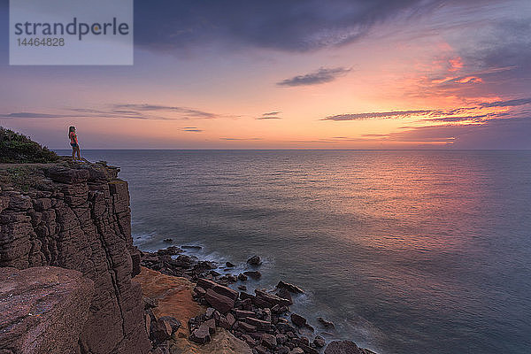 Ein Mädchen betrachtet den Sonnenuntergang von einer Klippe aus  Insel Sant'Antioco  Provinz Sud Sardegna  Sardinien  Italien  Mittelmeer