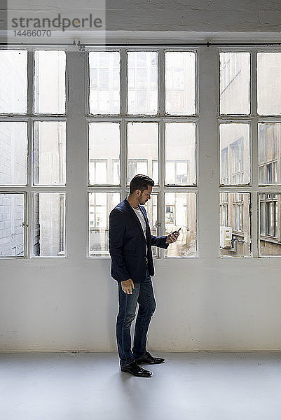 Geschäftsmann steht in einem Loft am Fenster und benutzt sein Handy