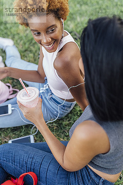 Zwei glückliche Freundinnen entspannen sich in einem Park und hören Musik