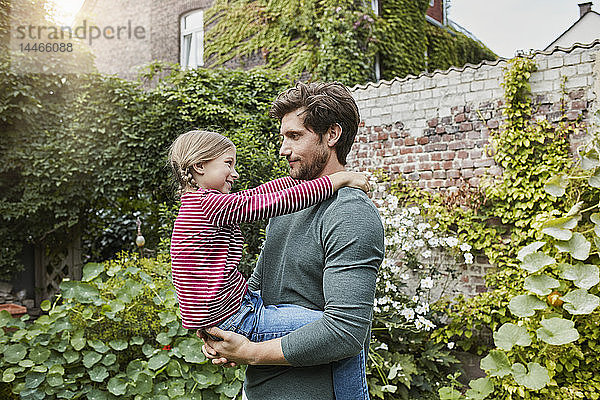 Vater trägt Tochter im Garten seines Hauses