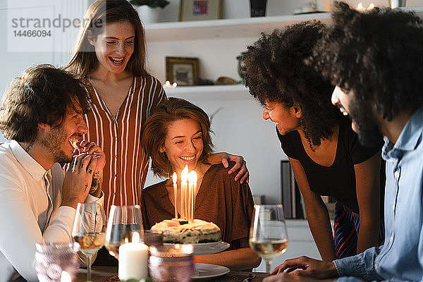 Freunde überraschen junge Frau mit einem Geburtstagskuchen mit brennenden Kerzen